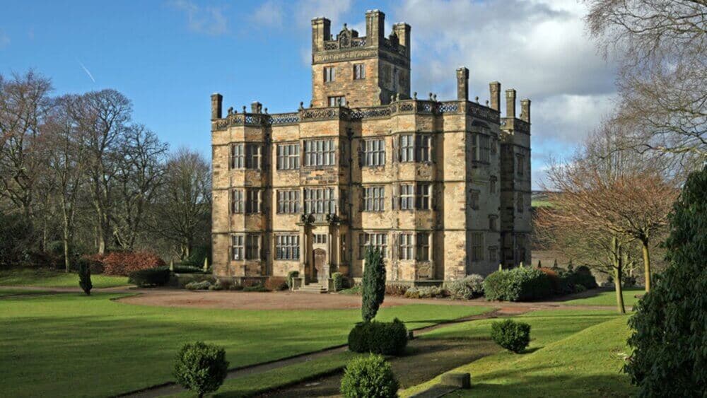 A historic, multi-story stone mansion with large windows, surrounded by manicured lawns and trees under a blue sky. - Home Instead