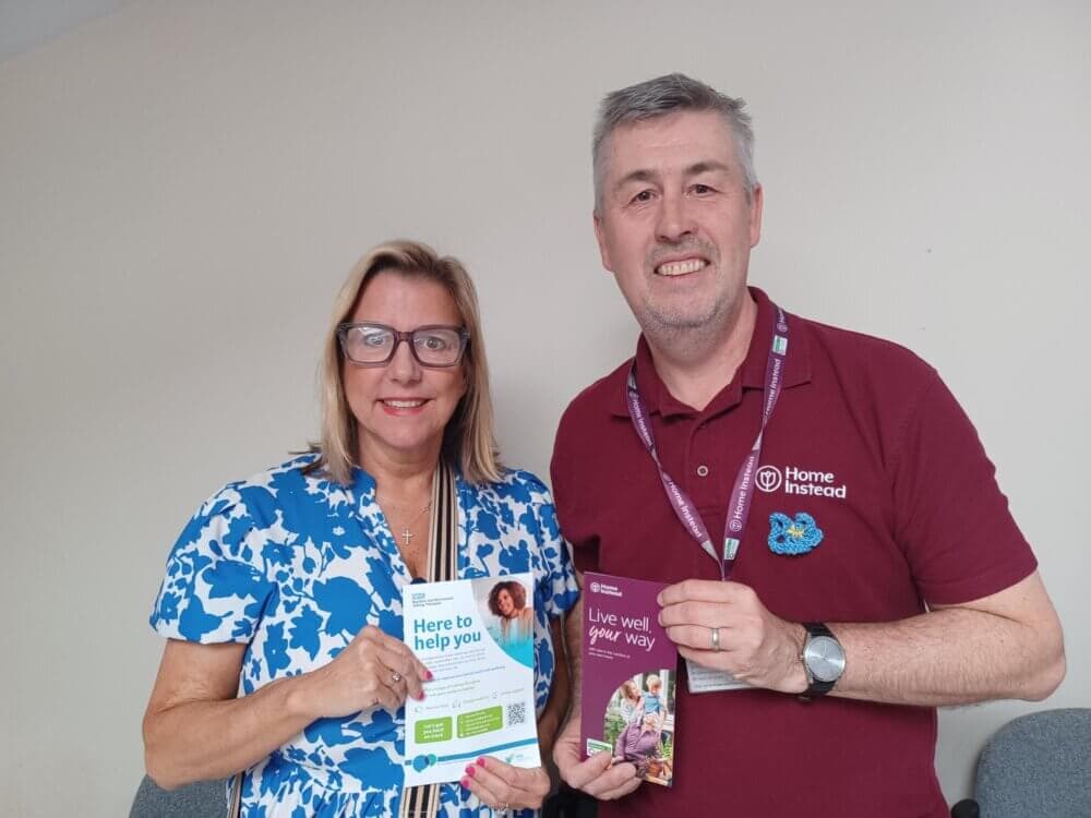 Two people holding brochures, one about help services and the other about living well, smiling in an indoor setting. - Home Instead