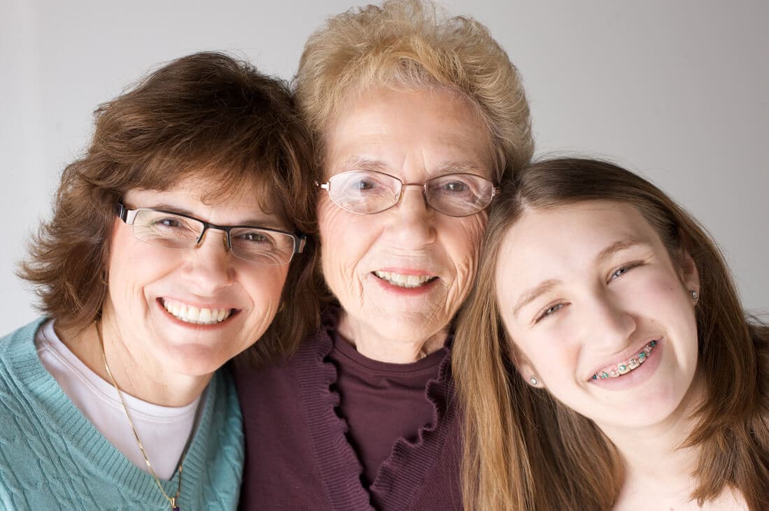 Three generations: a grandmother, daughter, and granddaughter smile together, the younger wearing braces. - Home Instead