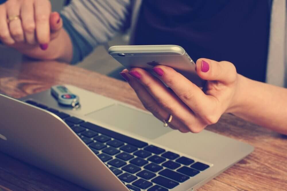 Person holding a smartphone and sitting at a desk with an open laptop and a USB stick on the keyboard. - Home Instead