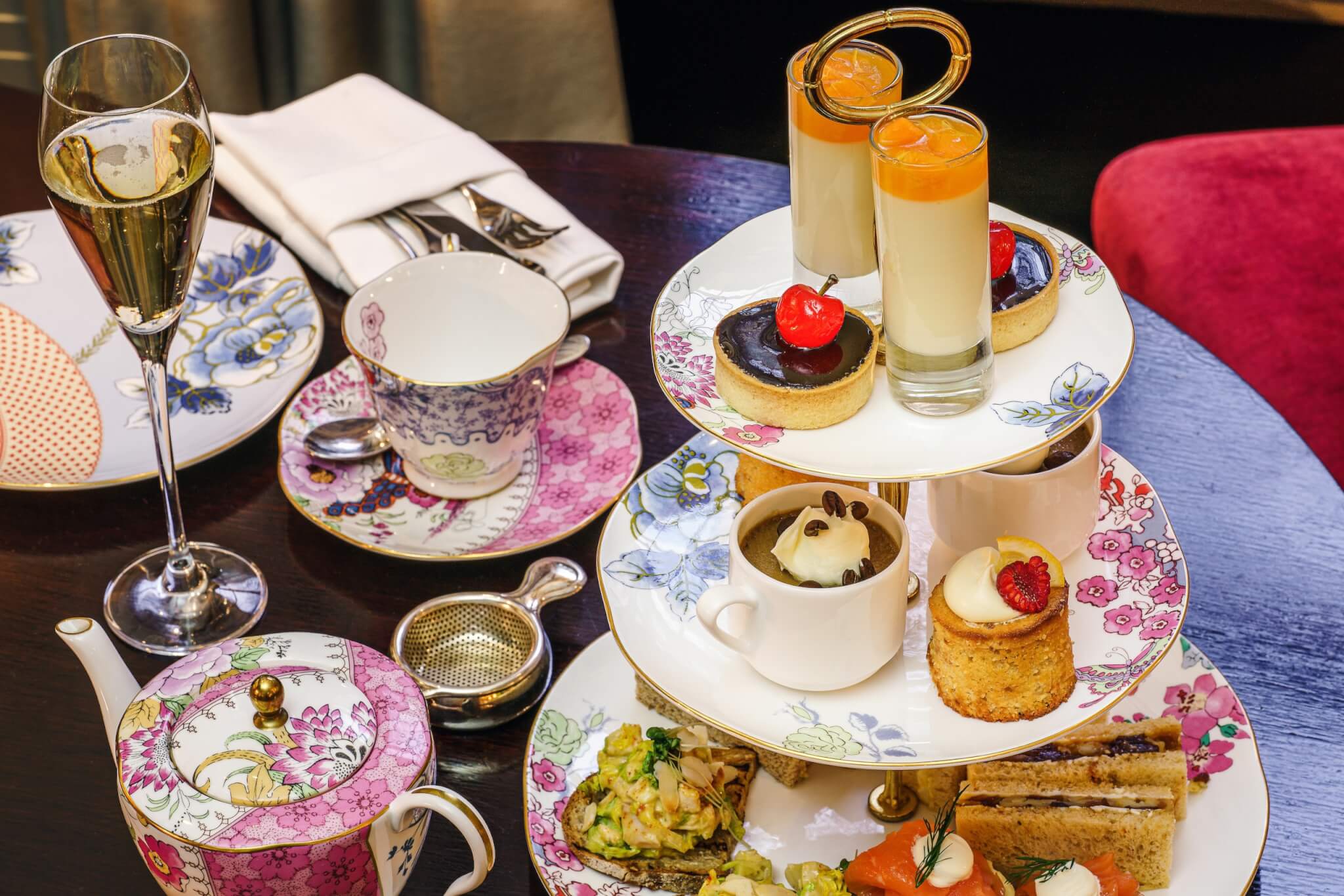 Elegant afternoon tea setting with tiered platter of desserts, sandwiches, a floral teapot, and champagne glasses. - Home Instead