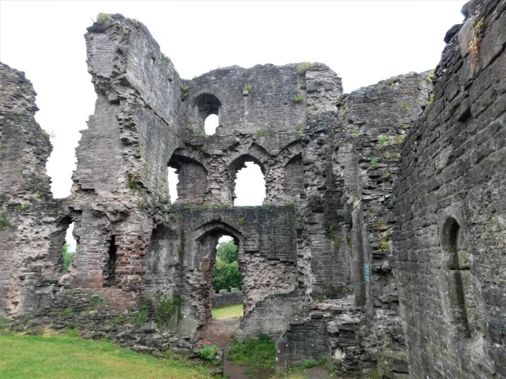 Stone ruins of an old building with arches and windows, surrounded by greenery under an overcast sky. - Home Instead