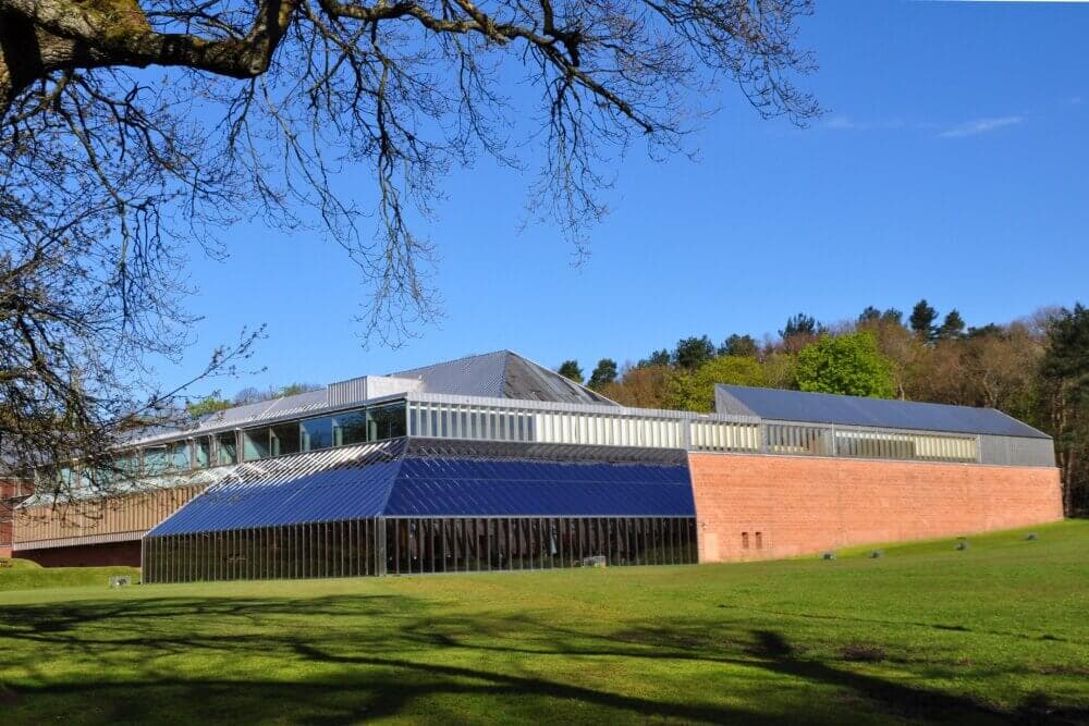A modern building with large glass windows, surrounded by greenery and trees under a clear blue sky. - Home Instead