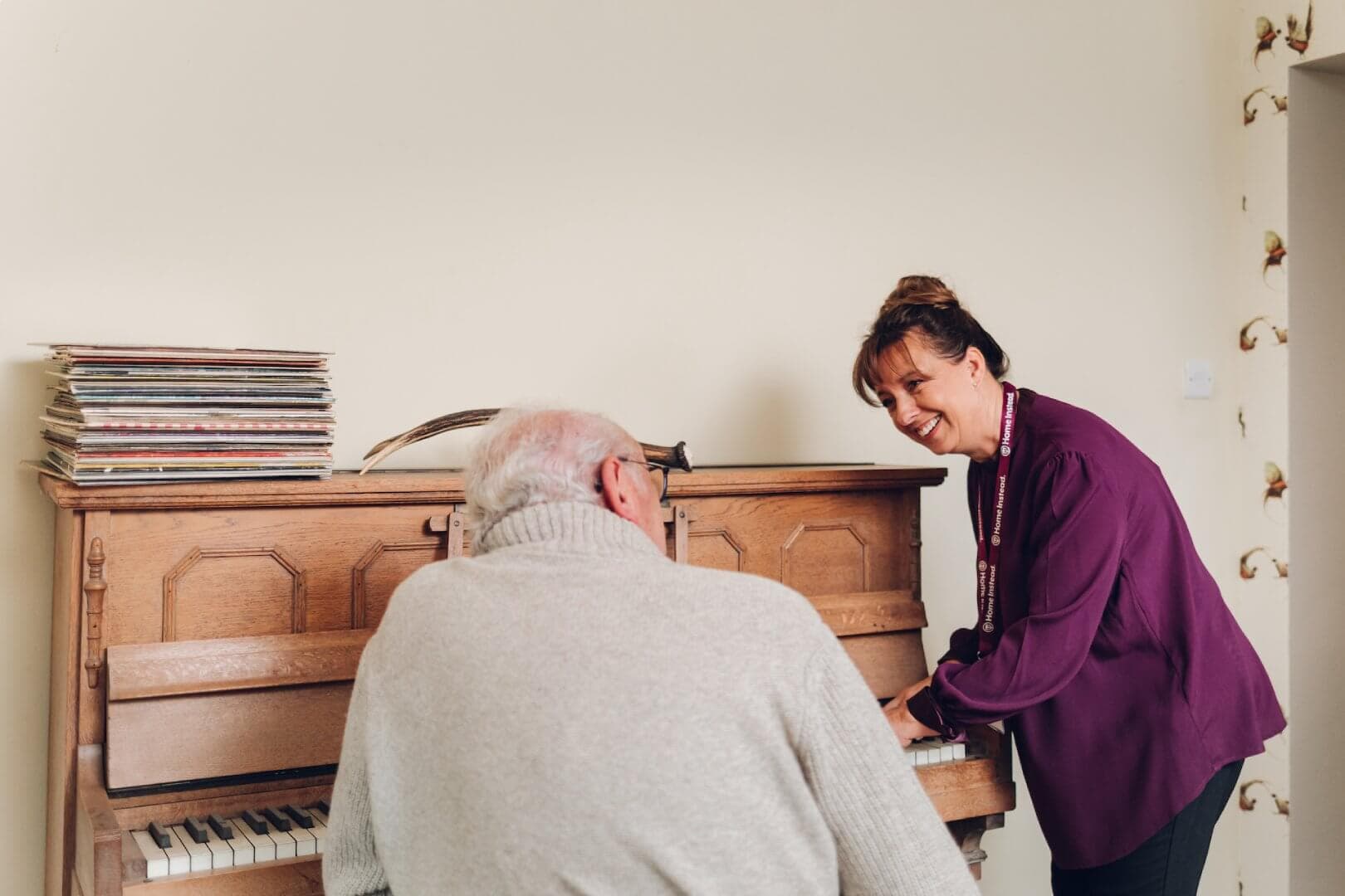 Woman in purple shirt and elderly man at a piano, smiling and engaging in a musical activity together. - Home Instead