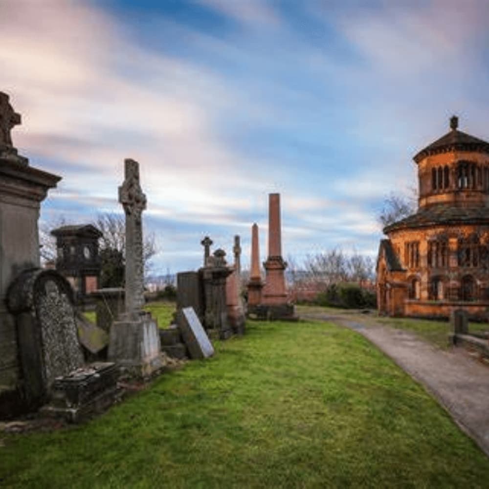Graveyard with old tombstones and a mausoleum under a cloudy sky at sunset. - Home Instead