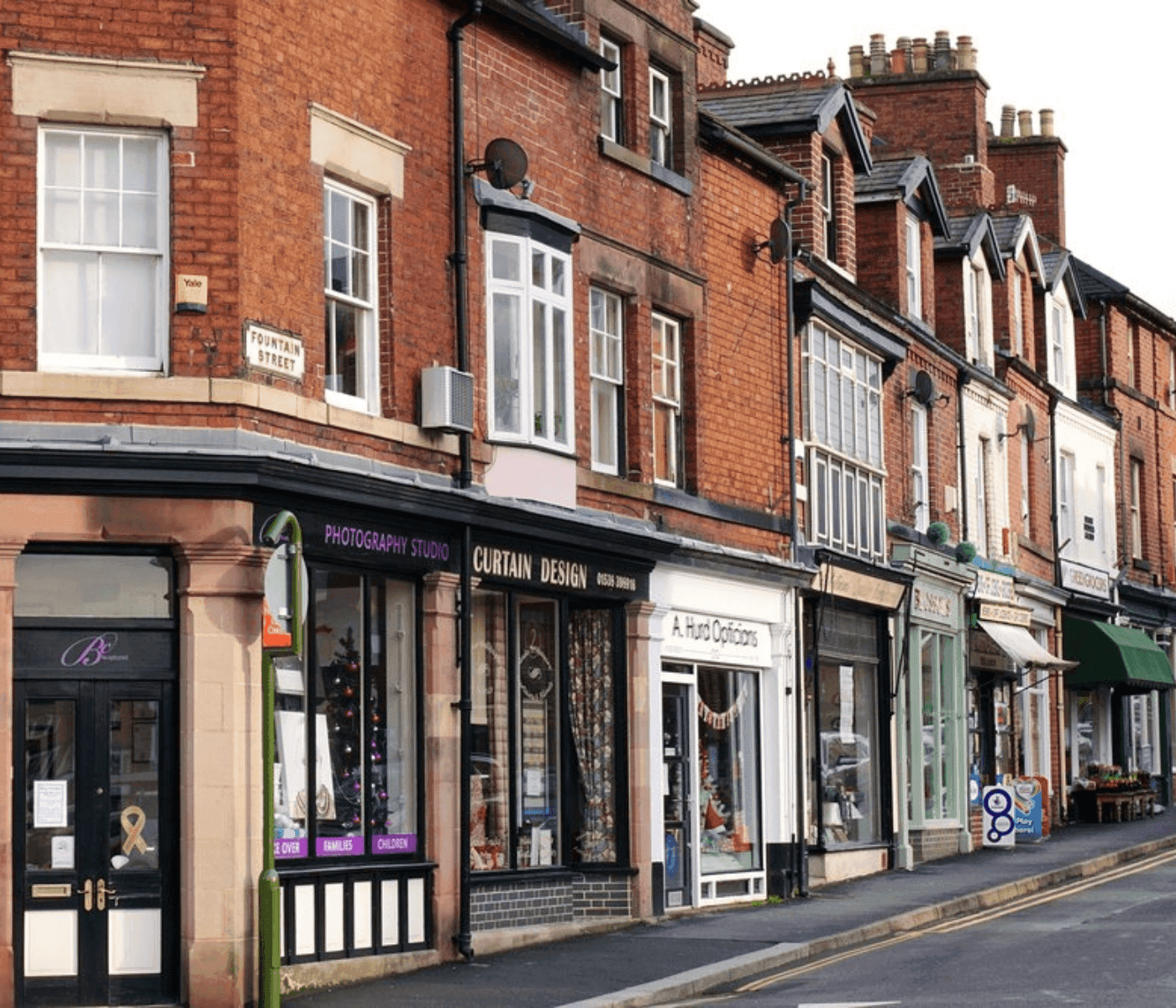 A street view showing various shops including a photography studio, curtain design shop, and optical store. - Home Instead