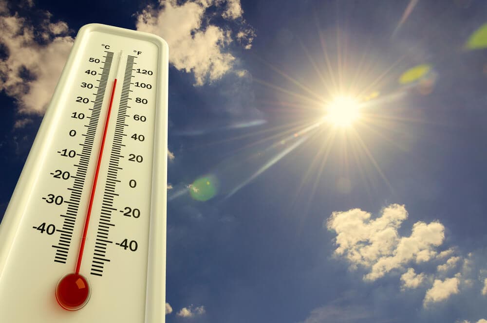 Thermometer showing high temperature against a bright, sunny sky with scattered clouds. - Home Instead