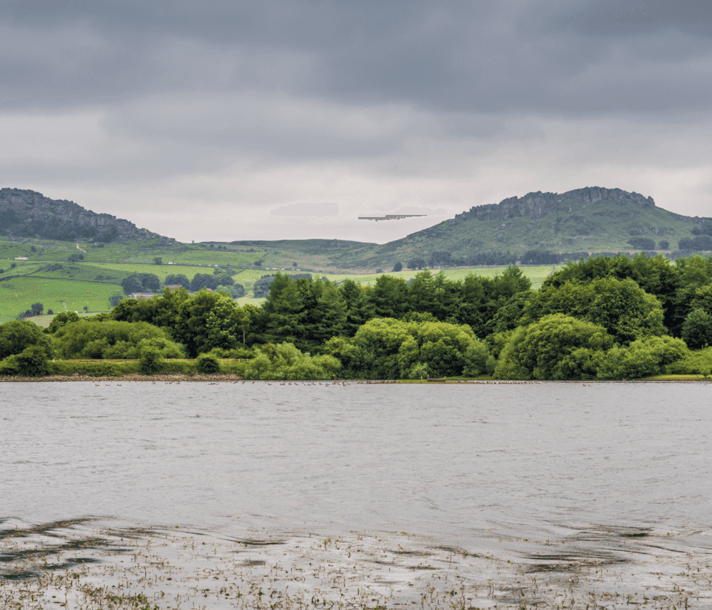 A calm lake with lush greenery on the shoreline, rolling hills, and a cloudy sky in the background. - Home Instead