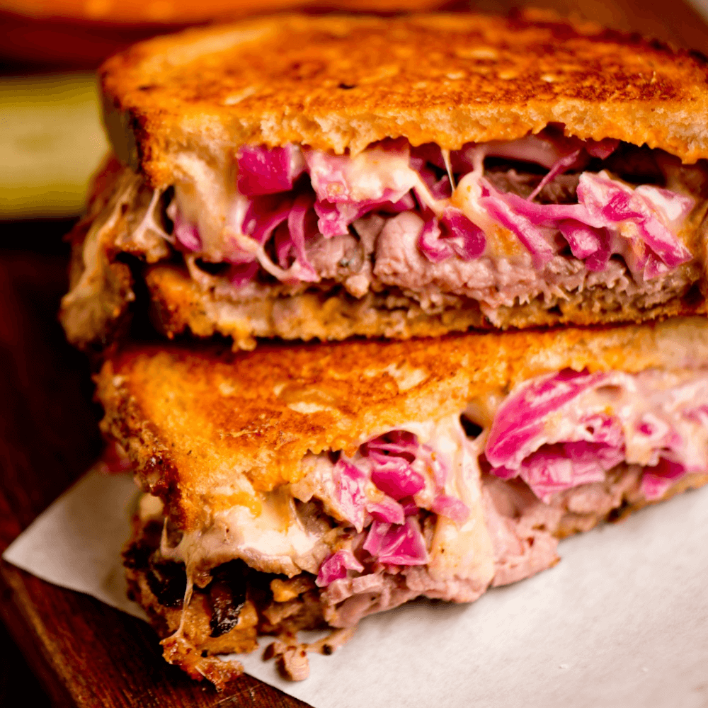 Close-up of a Reuben sandwich with melted cheese, corned beef, and sauerkraut, cut in half and stacked on top of each other. - Home Instead