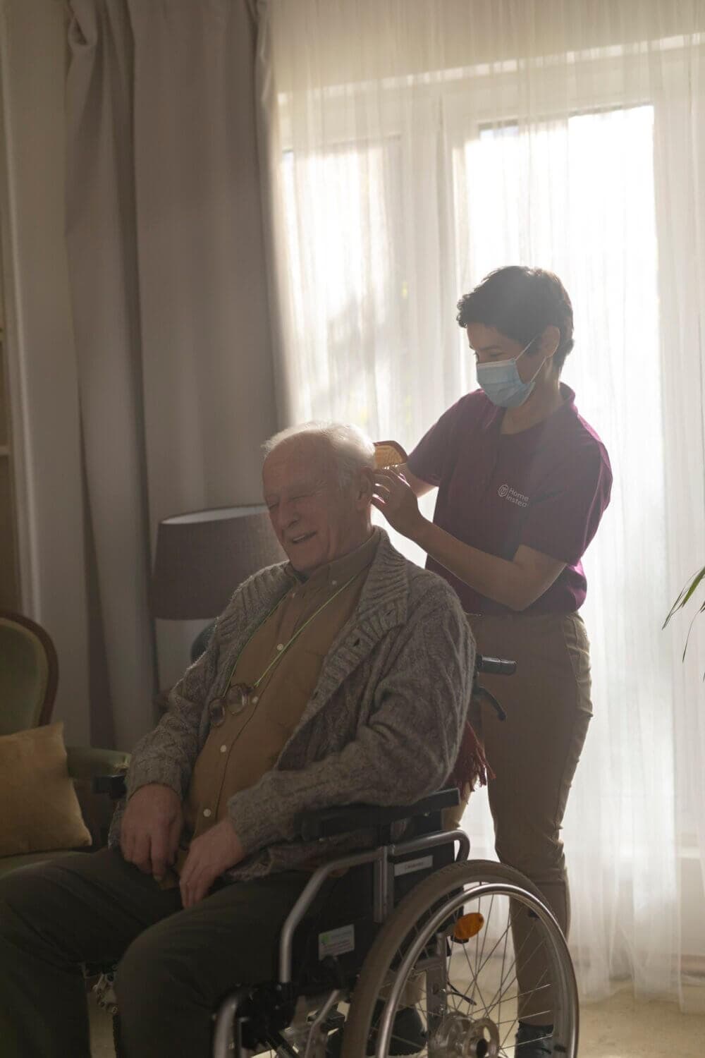 An older man and a caregiver share a laugh together in a warmly lit room. - Home Instead