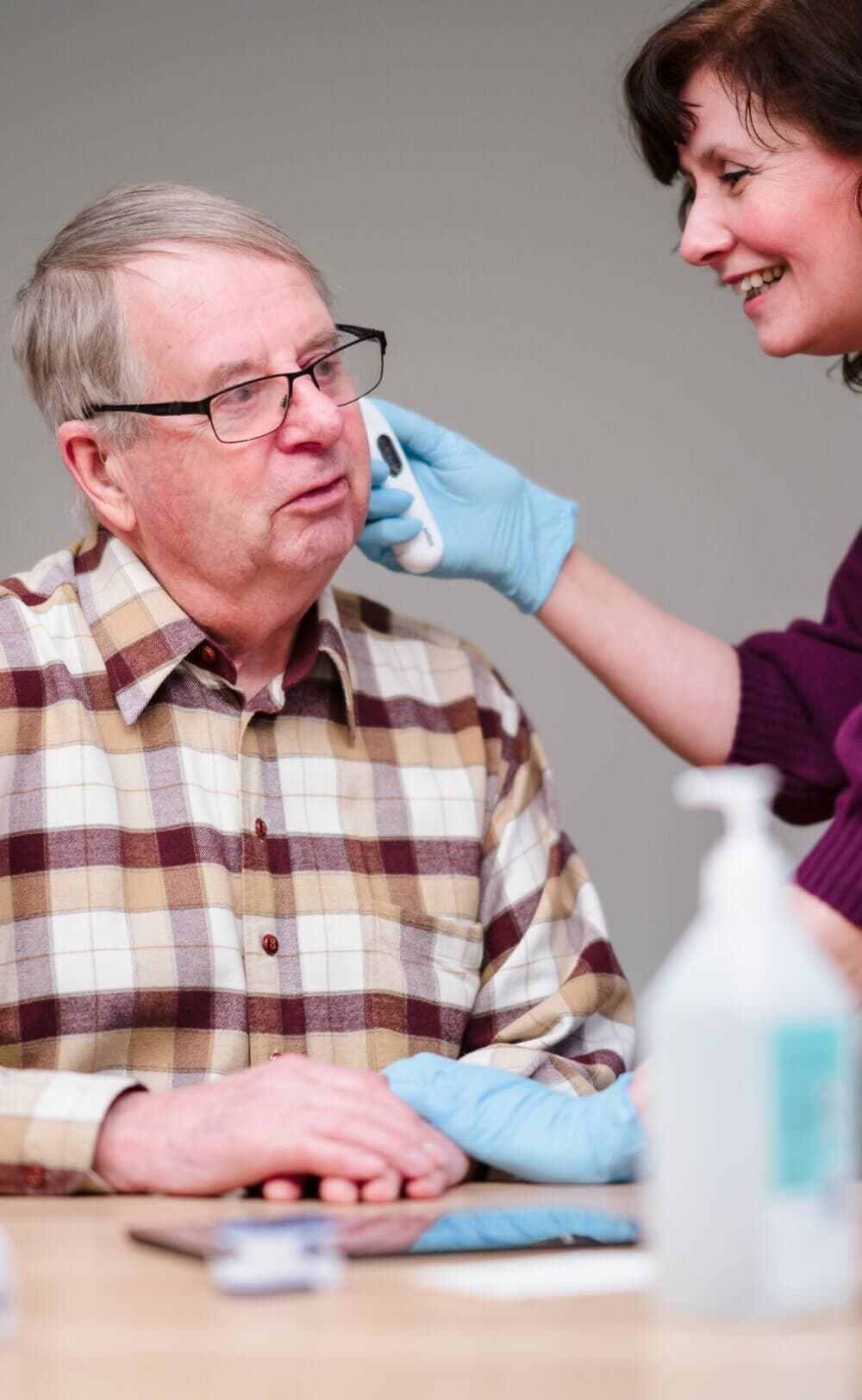 A caregiver checks the ear temperature of an elderly man using an electronic thermometer. - Home Instead