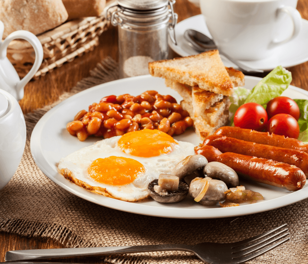 A plate with a full English breakfast: fried eggs, sausages, beans, mushrooms, toast, and cherry tomatoes. - Home Instead