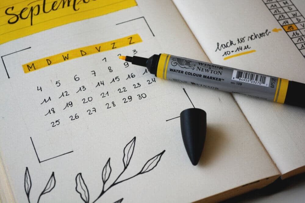 Open journal with a handmade September calendar, yellow highlights, and a black-capped yellow marker placed on it. - Home Instead