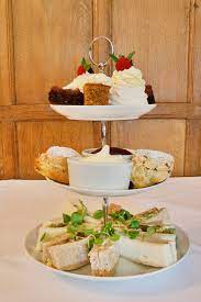 A three-tier dessert stand with sandwiches, pastries, and cakes, garnished with herbs on the bottom tier. - Home Instead