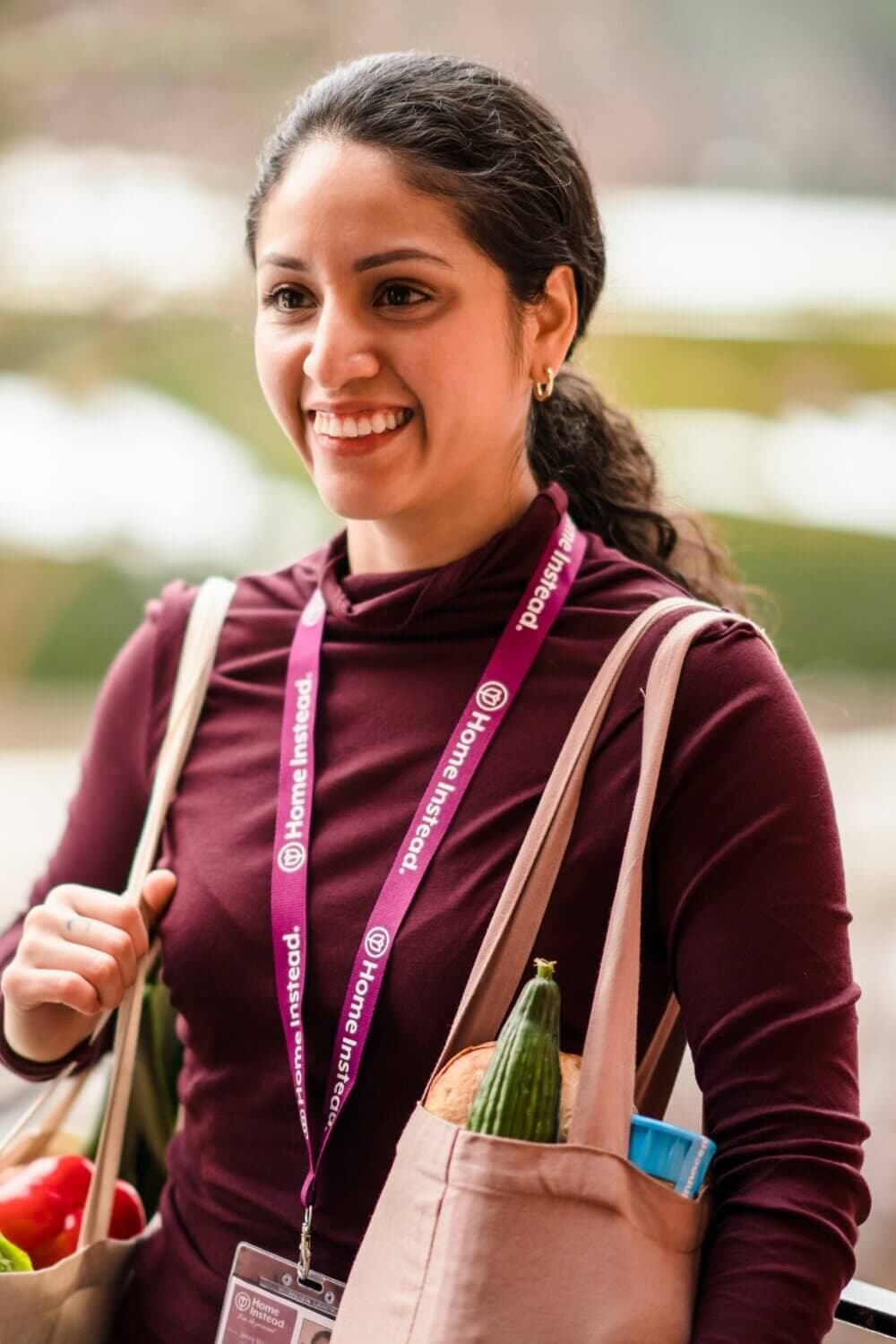 A Christchurch Care Professional with a lanyard, carrying grocery bags and smiling outdoors. - Home Instead Bournemouth & Christchurch