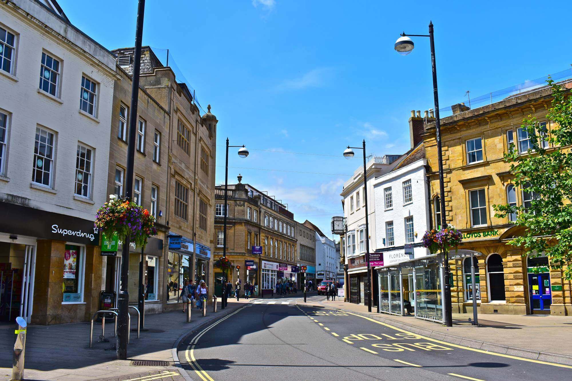 Street view of a small town with shops, street lamps, hanging flower baskets, and clear blue sky on a sunny day. - Home Instead