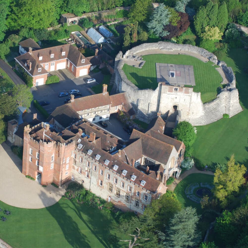Aerial view of a historic castle with surrounding gardens, stone walls, and adjacent buildings. - Home Instead