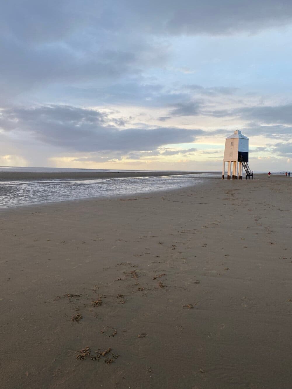 A sandy beach with a lifeguard tower on stilts under a cloudy sky at sunset. - Home Instead