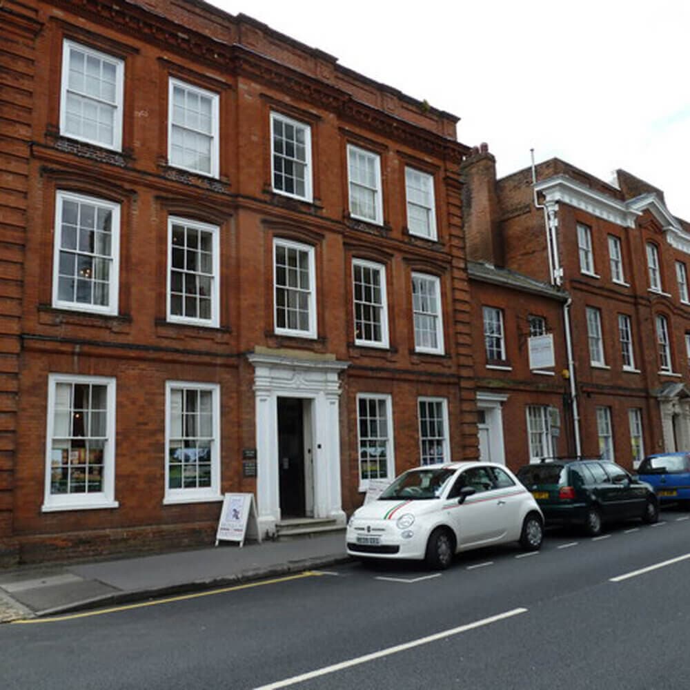 Street view of a row of three-story red brick buildings with cars parked in front on a cloudy day. - Home Instead