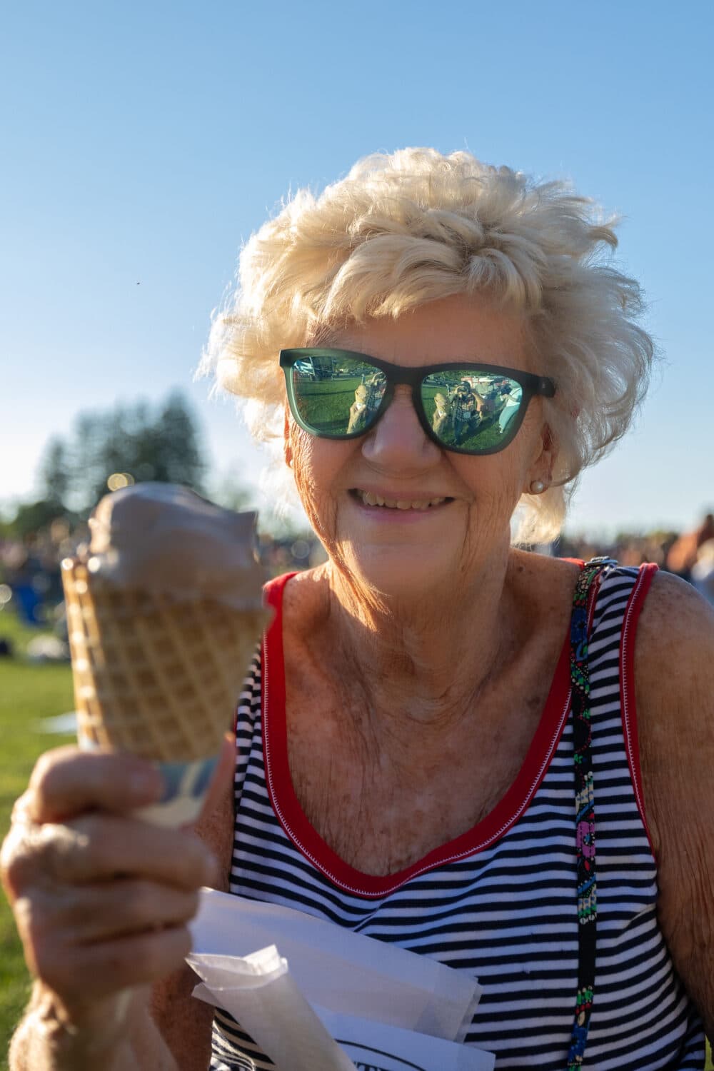 Smiling older woman in sunglasses holding an ice cream cone outdoors on a sunny day. - Home Instead