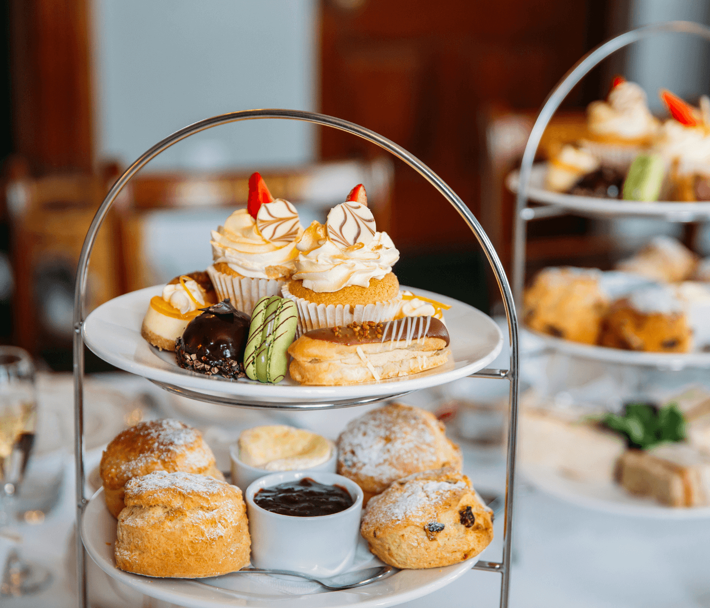 A three-tiered tray with assorted pastries, cupcakes, scones, and desserts displayed on a white tablecloth. - Home Instead
