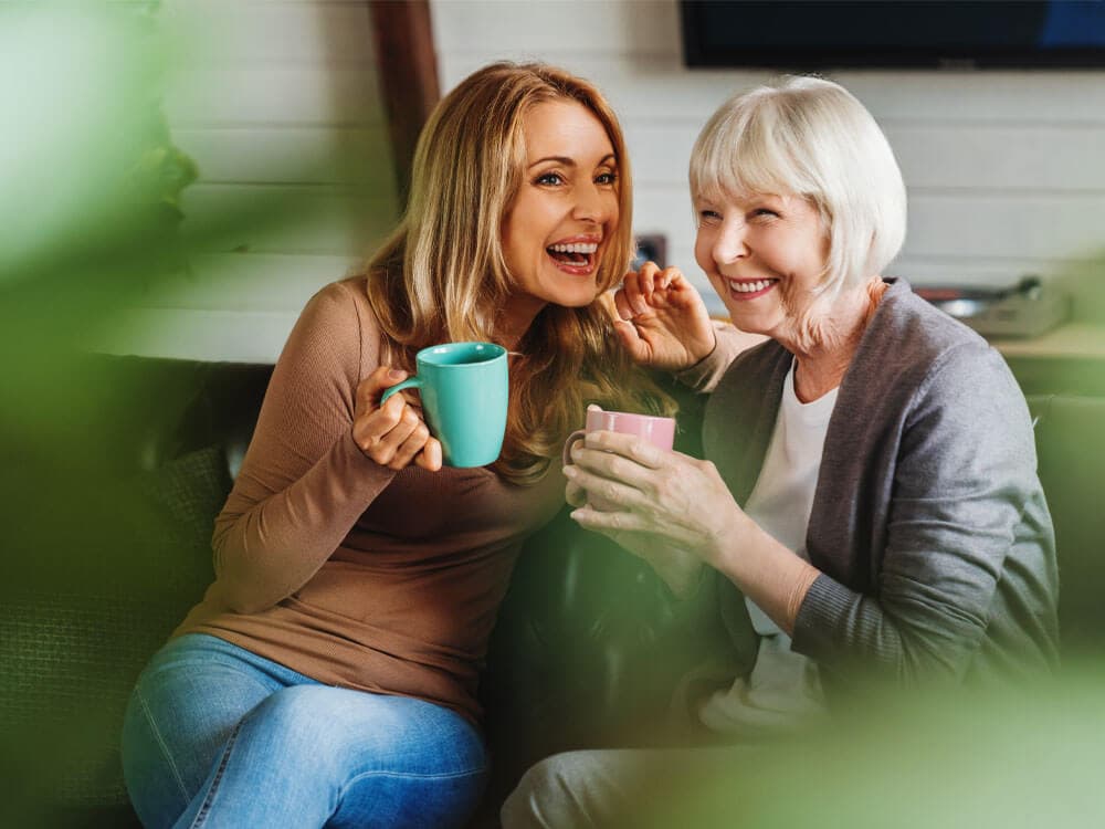 care pro and client sitting chatting next to each other on the sofa with a cup of tea