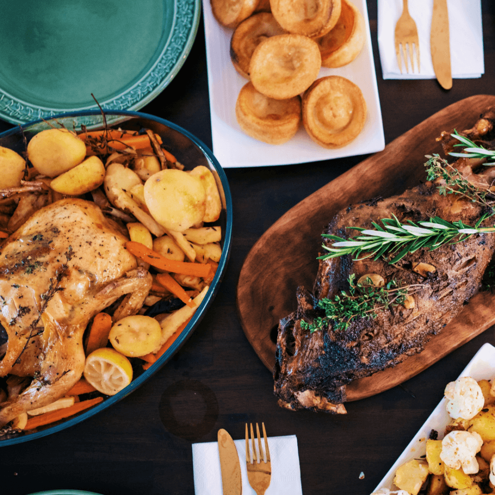 A table set with roasted chicken and vegetables, roast beef with rosemary, Yorkshire puddings, and other side dishes. - Home Instead