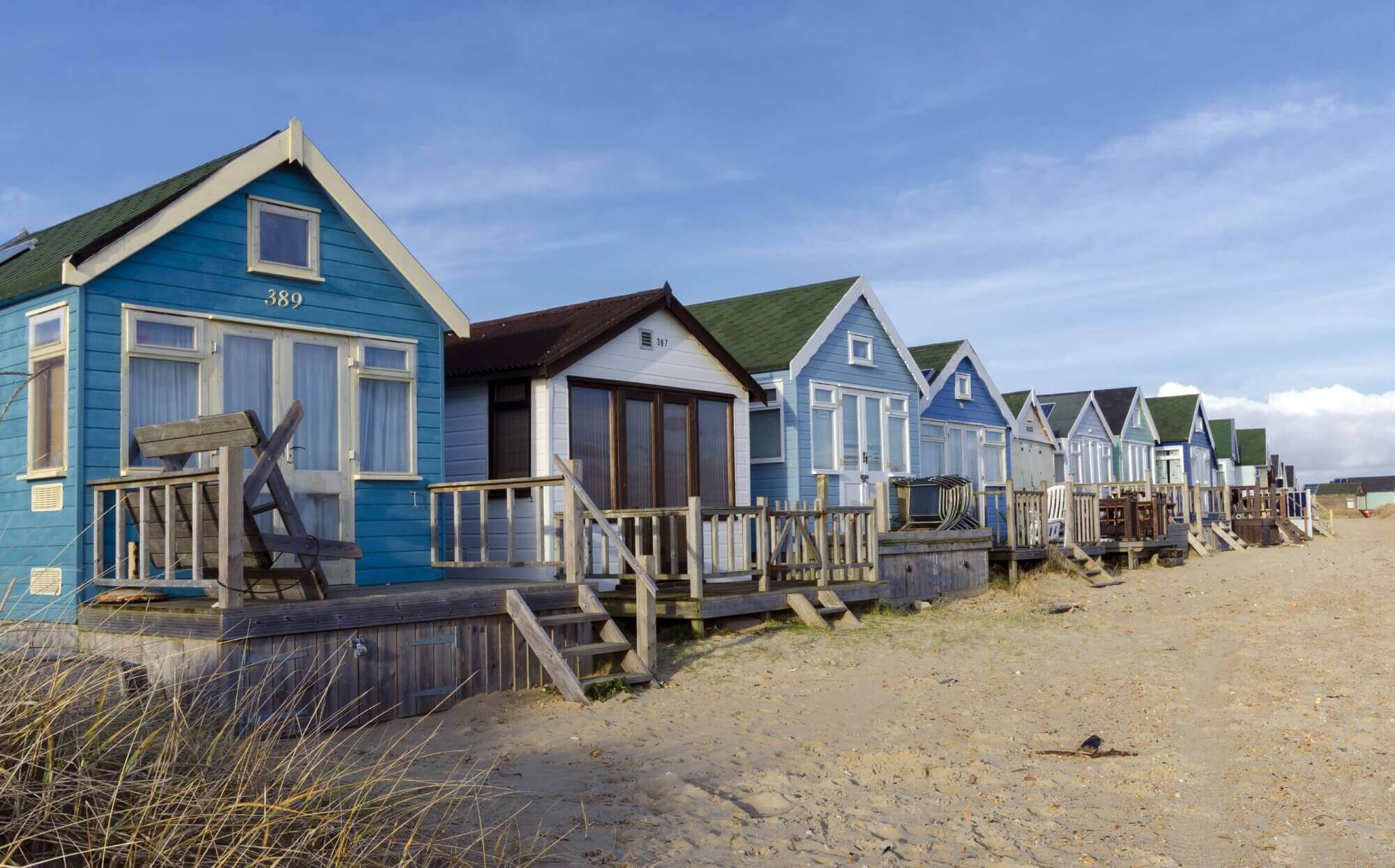 Colourful beachfront huts with wooden decks lined up along a sandy coastal area under a bright blue sky. - Home Instead Bournemouth and Christchurch