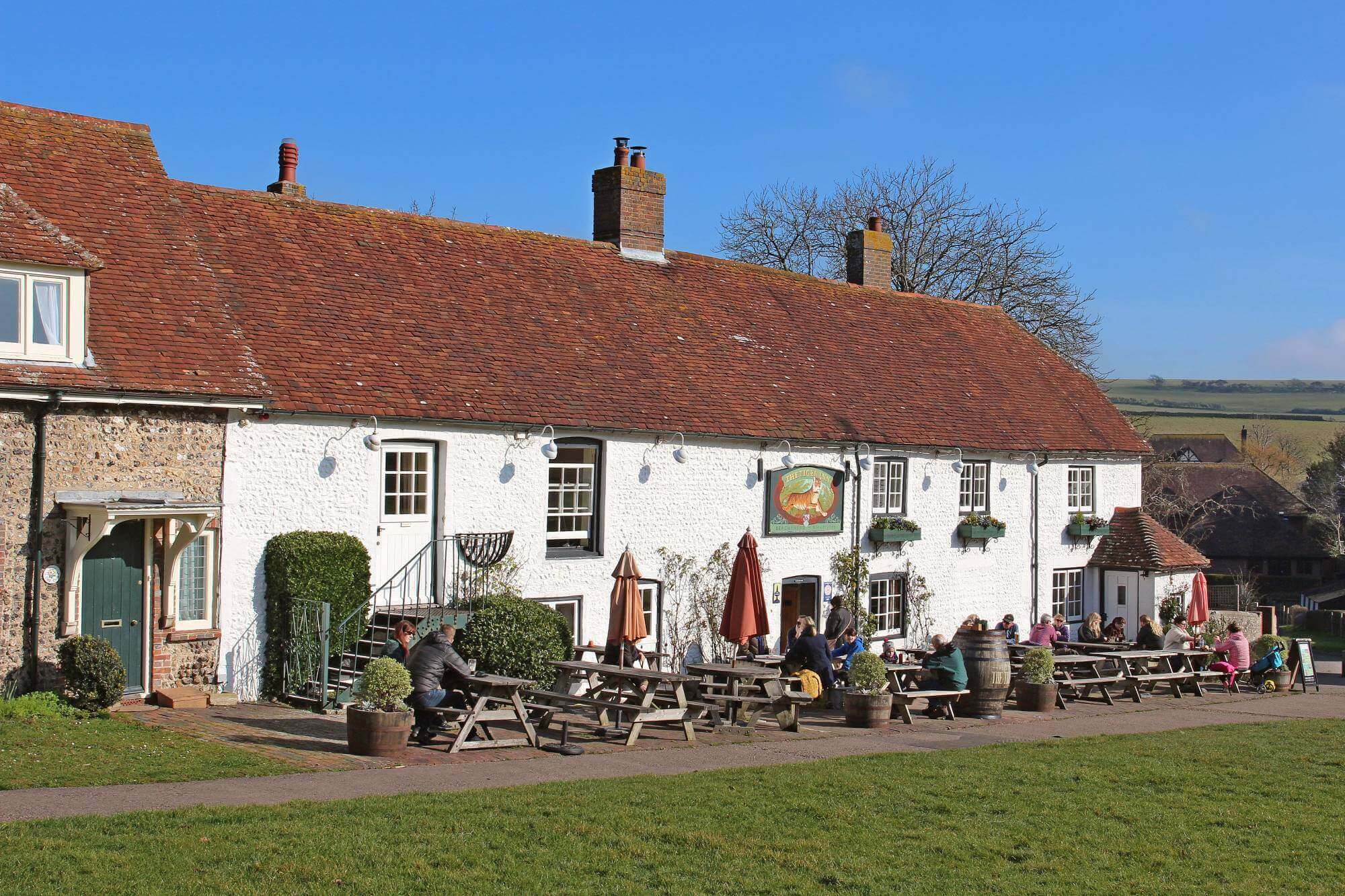 A quaint countryside pub with people sitting at outdoor wooden tables on a sunny day. - Home Instead