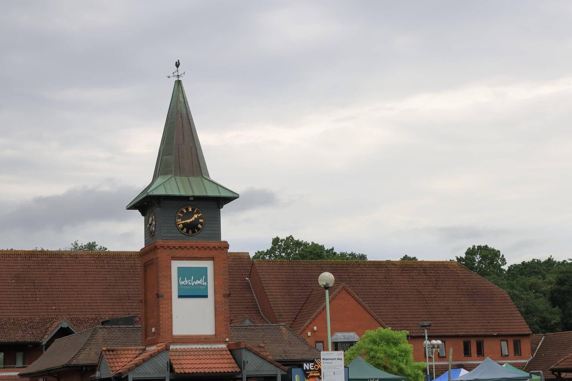 Clock tower with a green spire atop a brick building under a cloudy sky; a sign reads "Whiteley". - Home Instead Southampton
