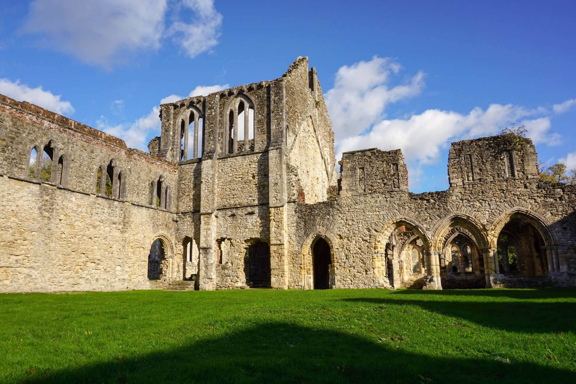Ancient stone ruins with arched doorways and windows under a bright blue sky with clouds, surrounded by green grass. - Home Instead Southampton