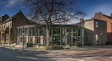 A modern, glass-fronted building with a tree in front, surrounded by older brick structures under a blue sky. - Home Instead