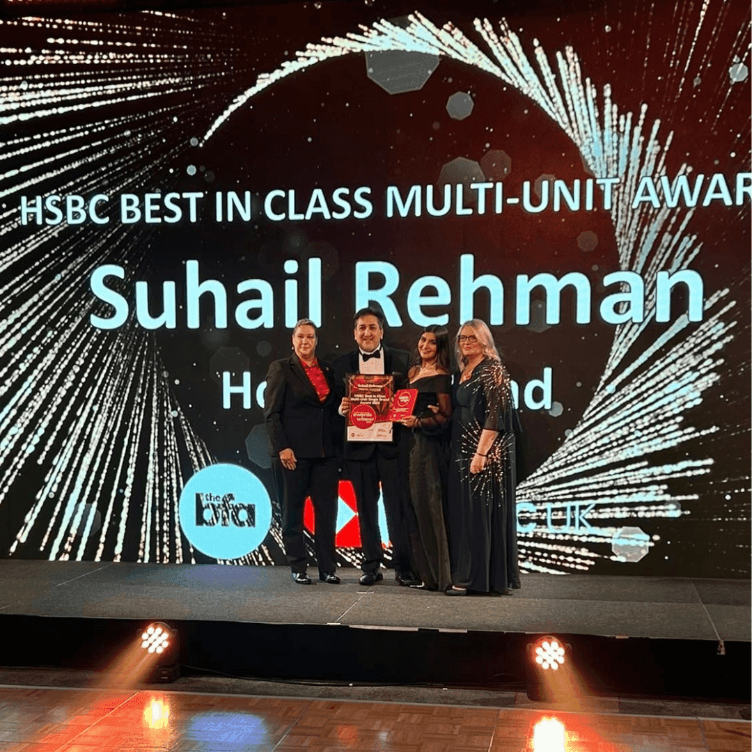 Group of four people on stage holding an award, with a screen behind them reading "HSBC Best in Class Multi-Unit Award. - Home Instead