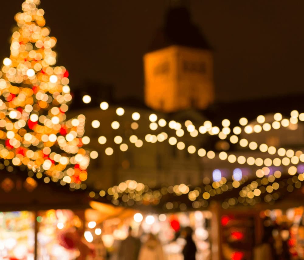 Blurred festive scene with illuminated Christmas tree and string lights, warm atmosphere, and people in the background. - Home Instead