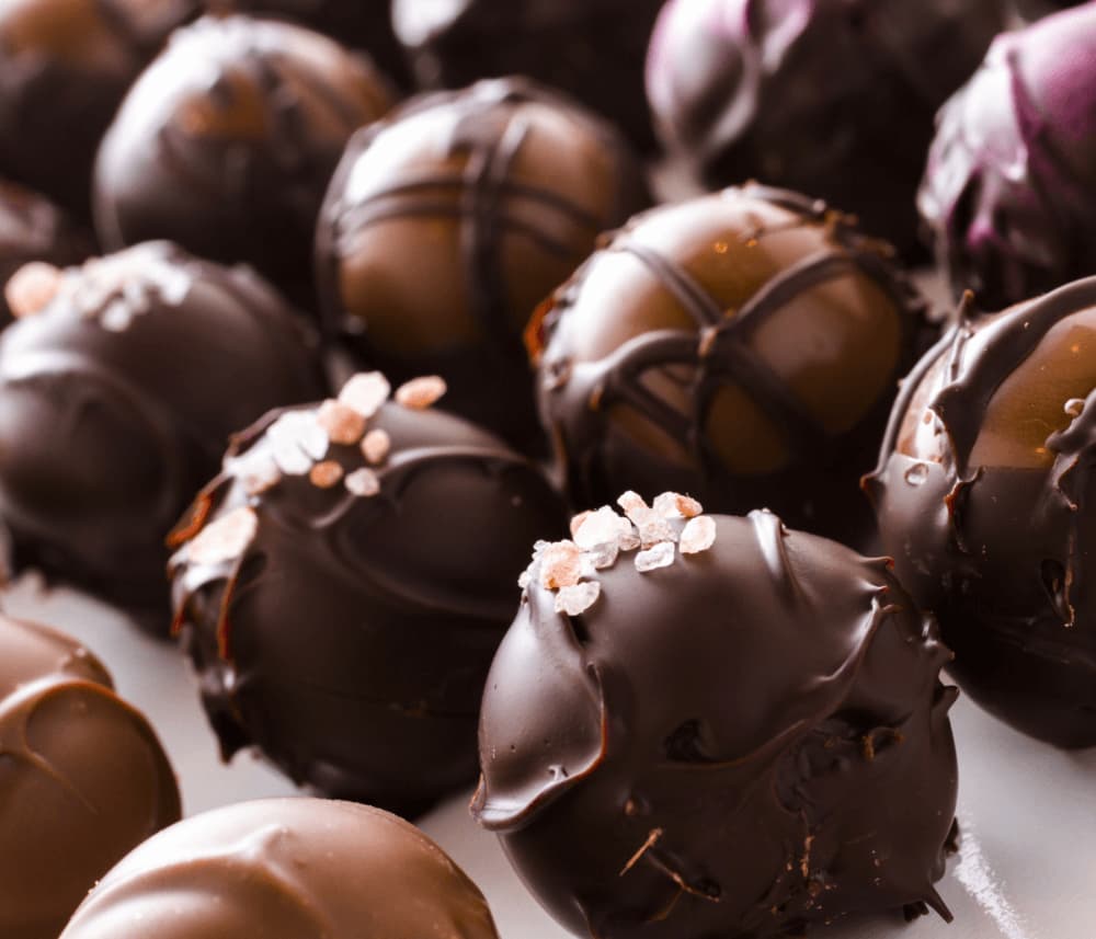 Close-up of various chocolate truffles with different toppings and drizzles, arranged in a pleasing pattern. - Home Instead