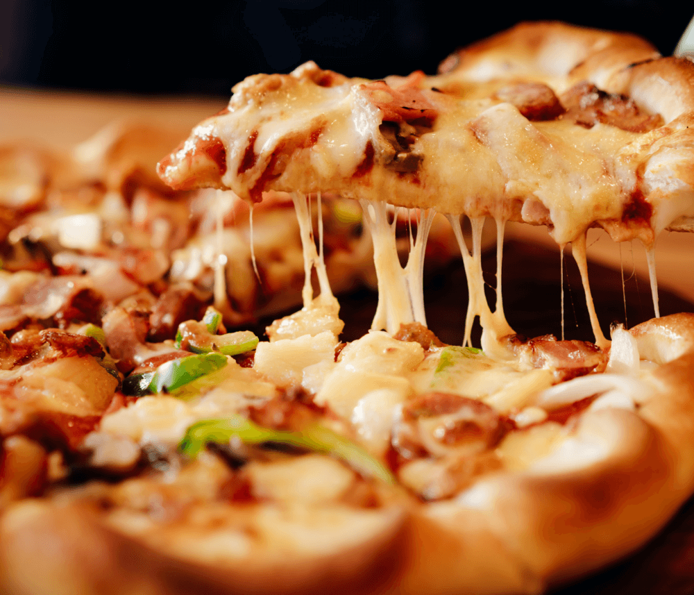Close-up of a cheesy pizza slice being lifted, showing melted cheese, vegetables, and meat toppings on a thick crust. - Home Instead