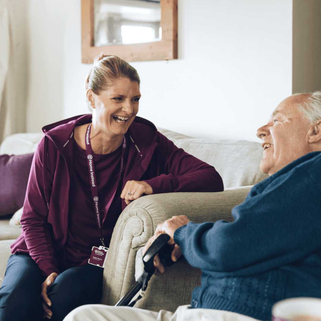 Female Care Professional and a male client laughing sitting on a sofa