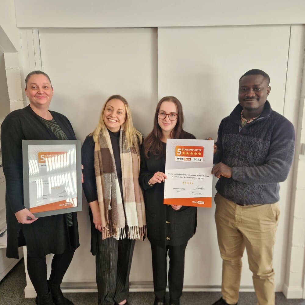 Four people smiling and holding a framed certificate and an award placard in an office setting. - Home Instead