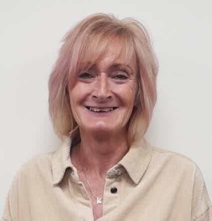Smiling woman with light blonde hair, wearing a beige collared shirt against a plain white background. - Home Instead