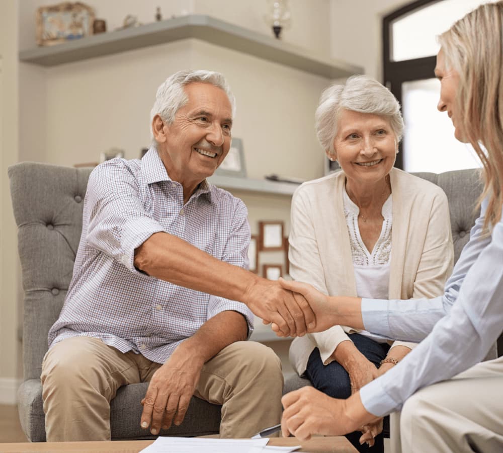 Elderly couple sitting on a couch, smiling and shaking hands with a woman in an office setting. - Home Instead