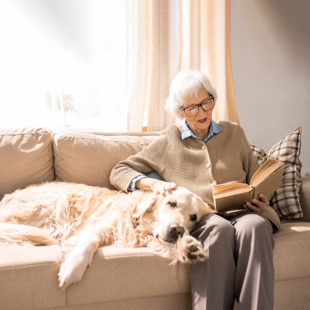 lady sat on the sofa reading a book with her dog lying comfortably next to her