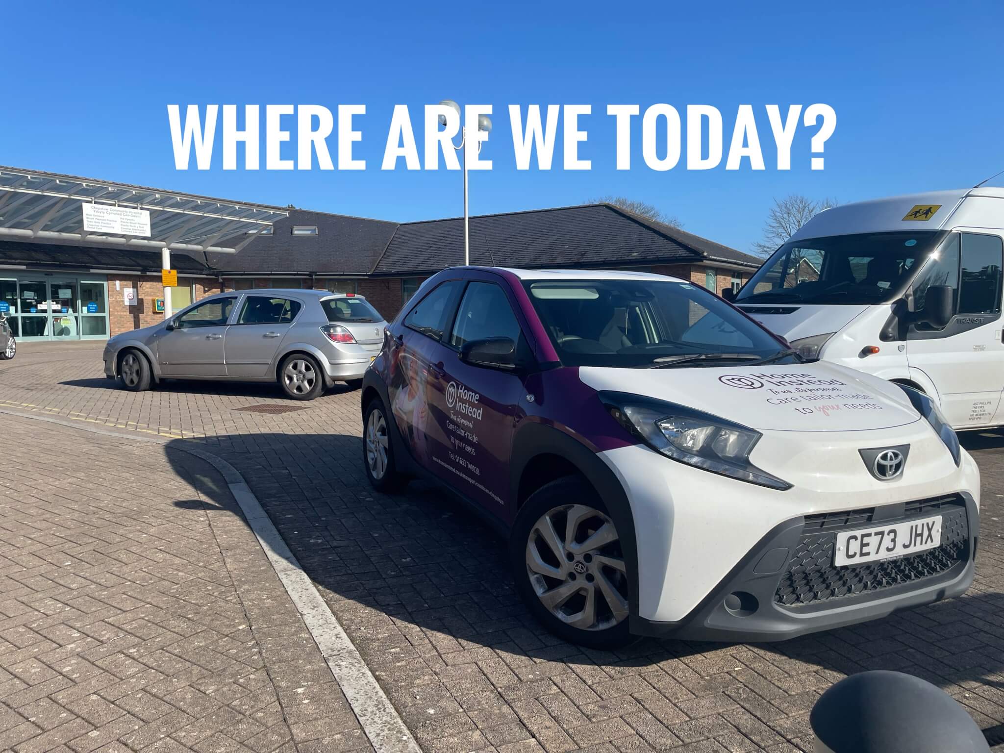 A purple and white car parked in front of a building with the text "WHERE ARE WE TODAY?" above it. - Home Instead