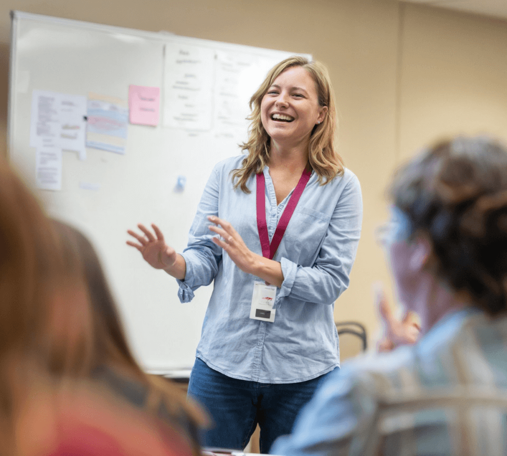 Engaging the community with workshops, a smiling lady leading a session with a white board behind her and audience members in the front of the photo