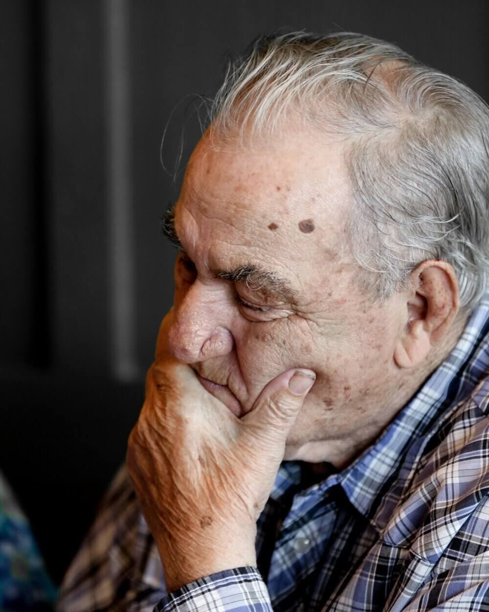 Elderly man with hand on chin, deep in thought, wearing a plaid shirt. - Home Instead