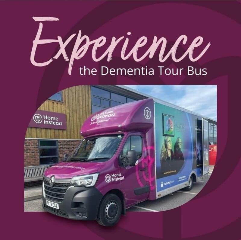 A purple Dementia Tour Bus in front of a building with a "Home Instead" logo and "Experience the Dementia Tour Bus" text. - Home Instead