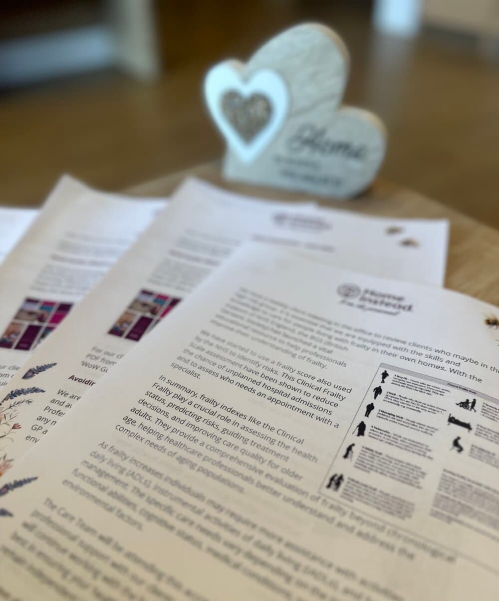 Close-up of printed documents on a surface, with a blurred heart-shaped ornament in the background. - Home Instead