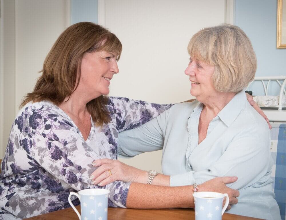 Home Instead client and her daughter hug at the table
