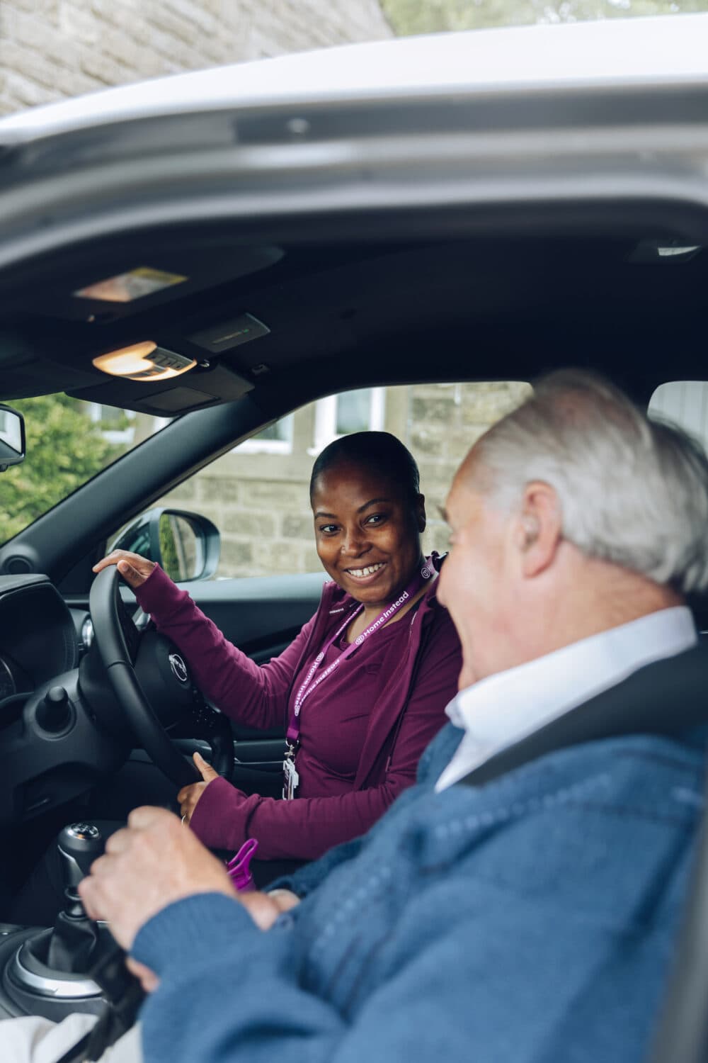 A smiling woman in a car talks to an elderly man sitting in the passenger seat. - Home Instead