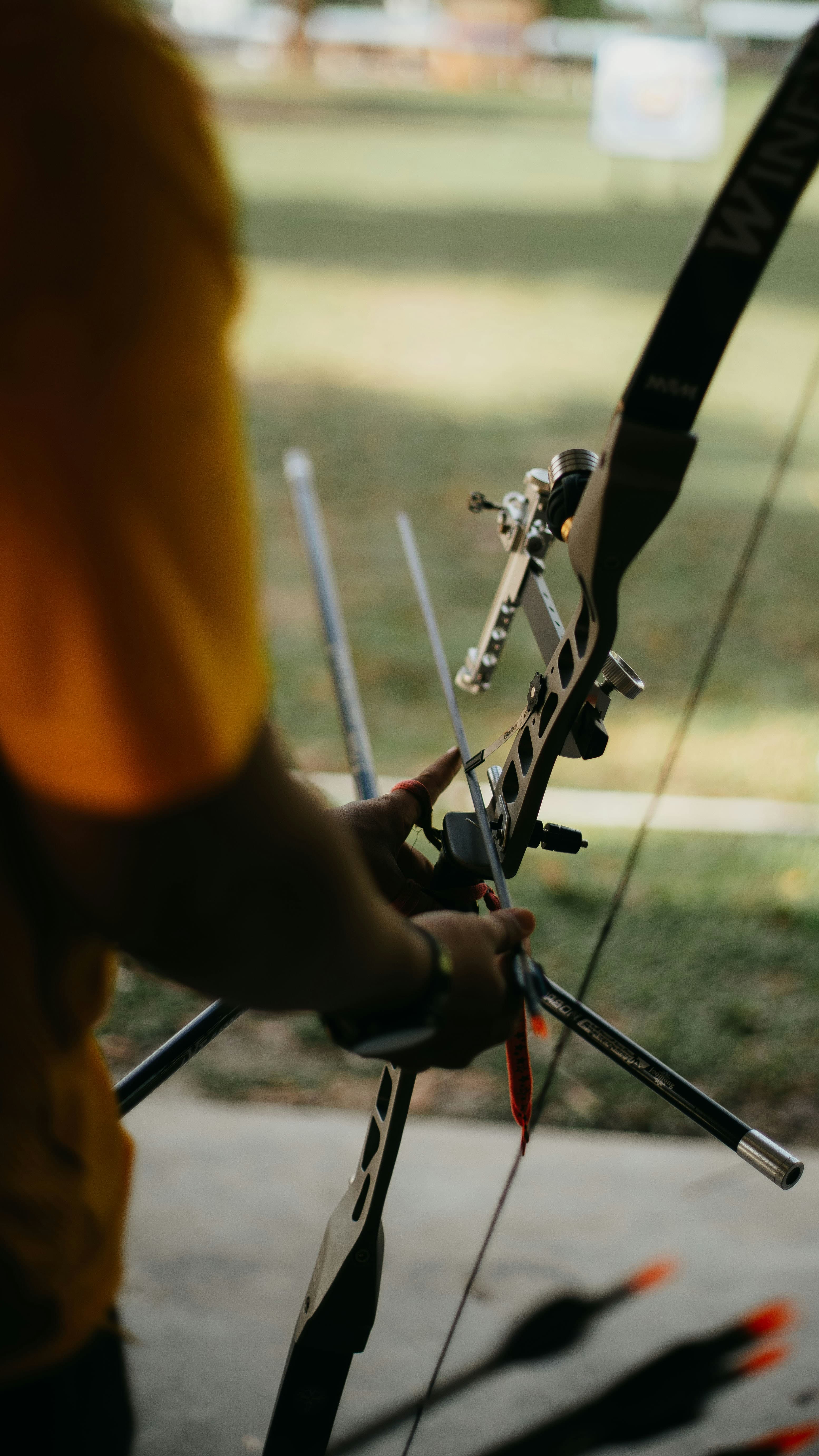 Person in yellow shirt preparing to shoot a bow and arrow outdoors. - Home Instead