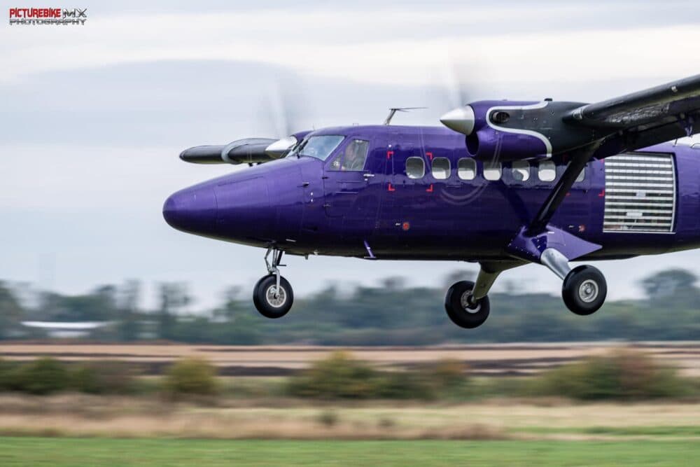 Purple passenger airplane landing on a grassy runway with blurred background. - Home Instead